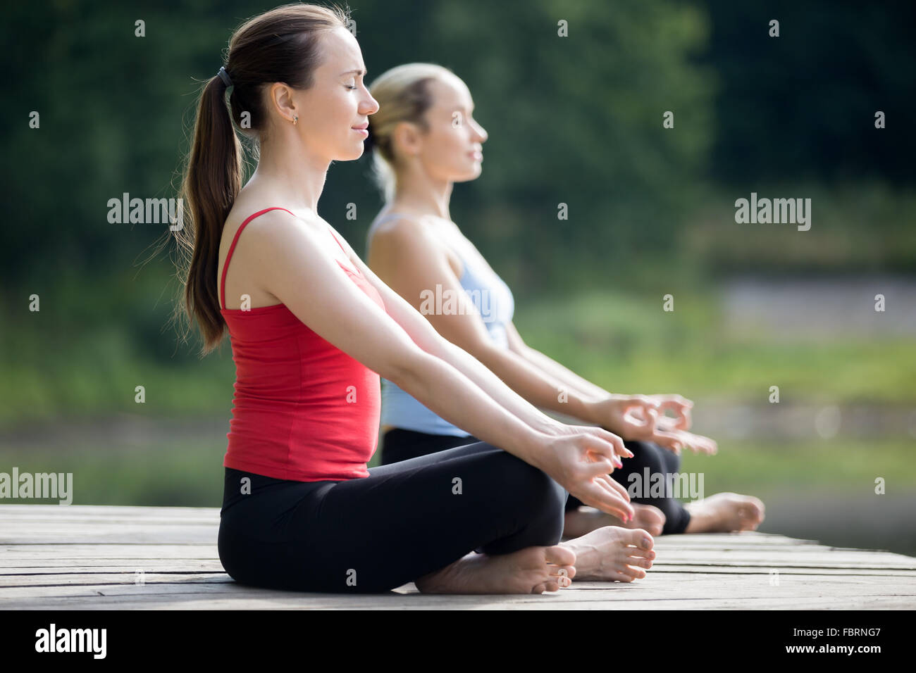 Due belle sporty montare le giovani donne in seduta facile (postura piacevole), Sukhasana, meditando con gli occhi chiusi, respirazione Foto Stock