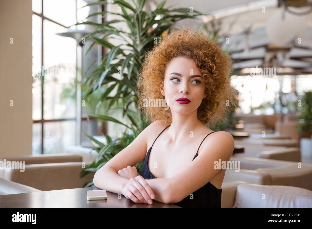 Ritratto di un giovane redhead donna con capelli ricci seduta al tavolo nel ristorante Foto Stock