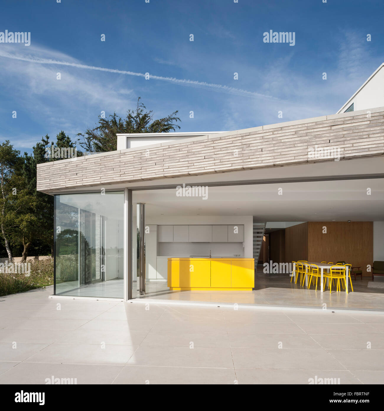 Vista della cucina dalla terrazza esterna con giallo Isola per cucina. Broombank, Costa di Suffolk, Regno Unito. Architetto: minestra Arch Foto Stock