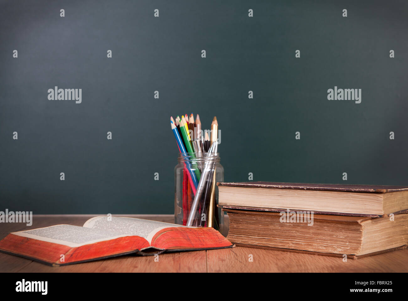 Quaderni e matite giacente su una tavola di legno a banchi di scuola di fronte a una lavagna verde Foto Stock
