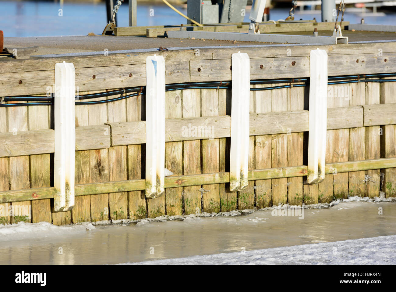 Close up al di fuori di un molo in legno come visto dal mare. È inverno e il mare ha congelato. Copertura di ghiaccio sul mare. Foto Stock