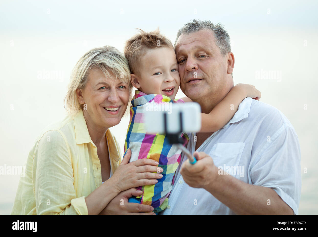 Felice nonni holding piccolo nipote di armi all'aperto e prendendo selfie stick picture insieme Foto Stock