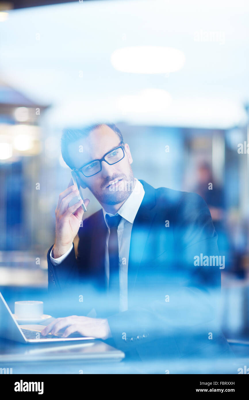 Imprenditore fiducioso che parla al telefono e di networking in cafe Foto Stock