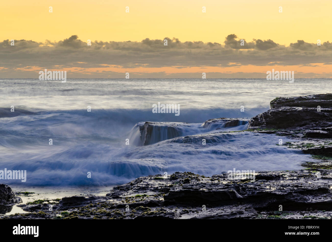 Il surf si riversa sul bordo di una piattaforma rocciosa mentre il sole sorge su una spiaggia di Sydney in Australia Foto Stock