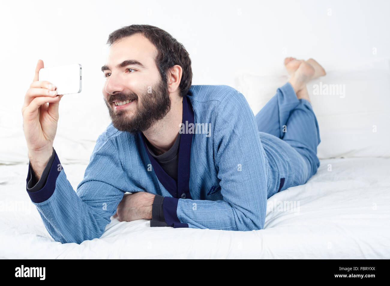 Uomo sorridente con pigiami prendendo un Selfie con uno smartphone Foto Stock