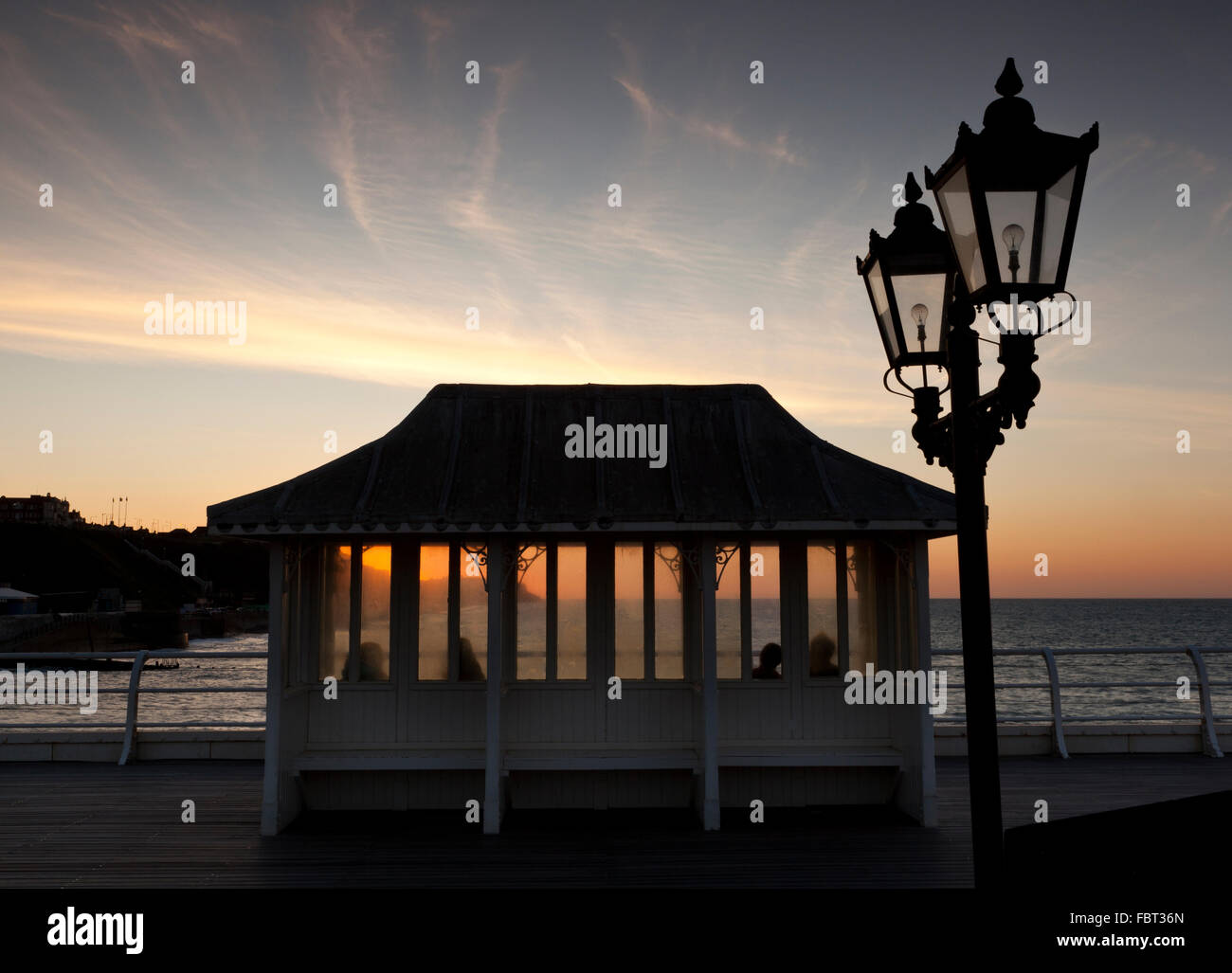Quattro persone sedute in uno del Vittoriano rifugi ornamentali su Cromer Pier, Norfolk, Inghilterra, Regno Unito a guardare il tramonto Foto Stock