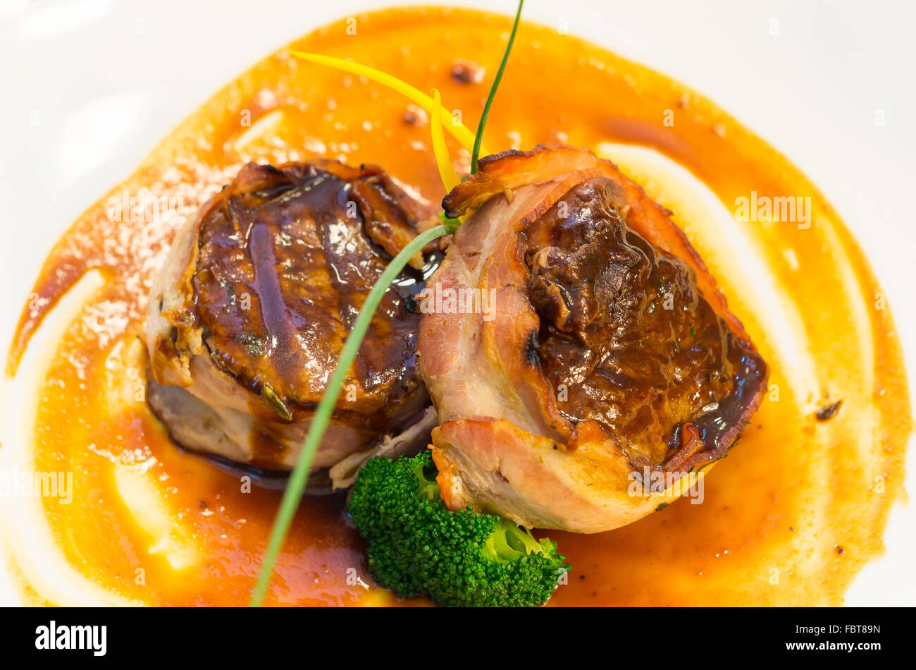 Deliziosa bistecca di filetto avvolto in pancetta e cotte alla perfezione, posta sulla piastra di colore arancione con alcuni elementi vegetali, elegante presentazione Foto Stock