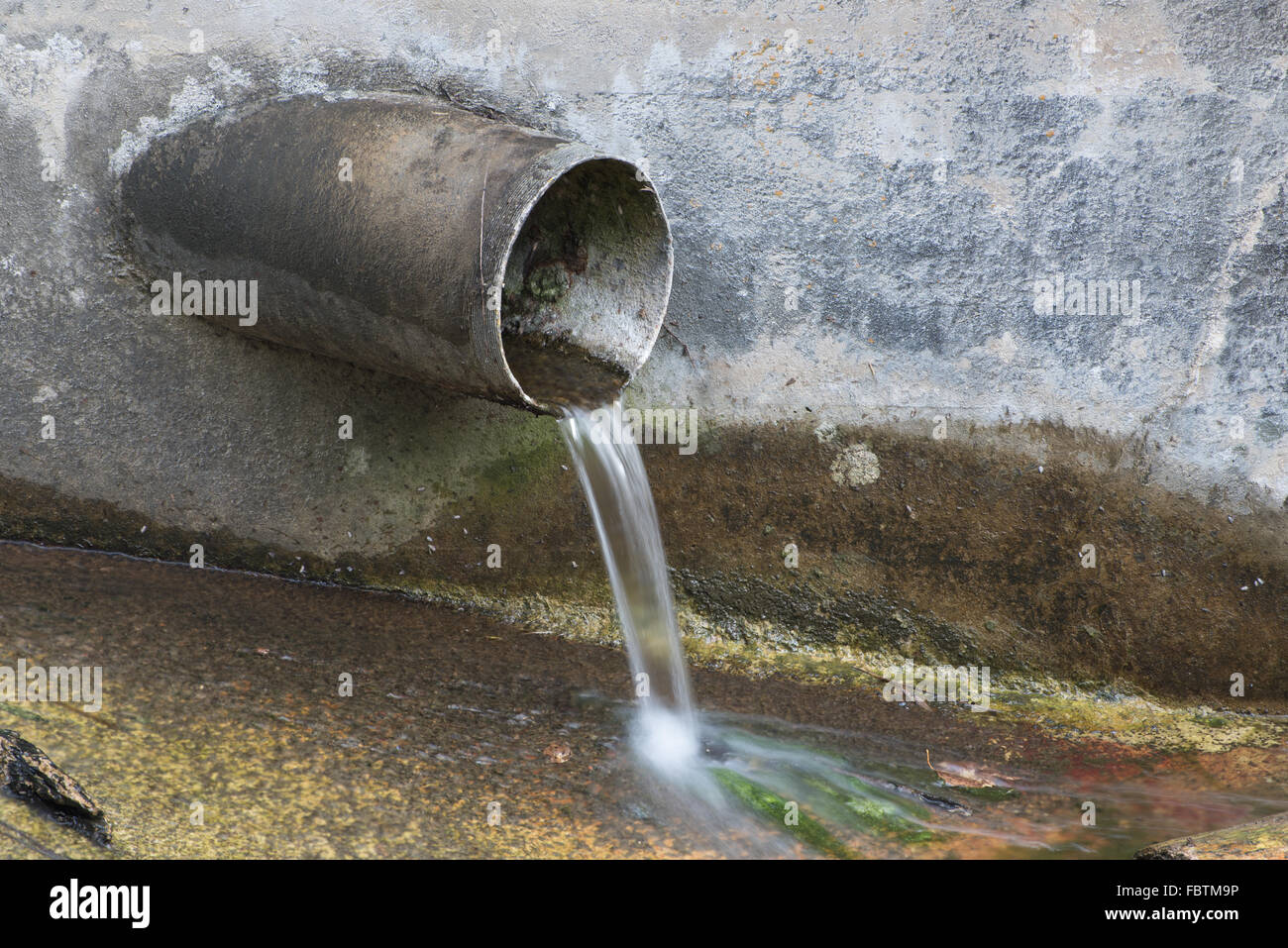 Tubo di drenaggio che sporge da una parete in cemento in un flusso. Foto Stock