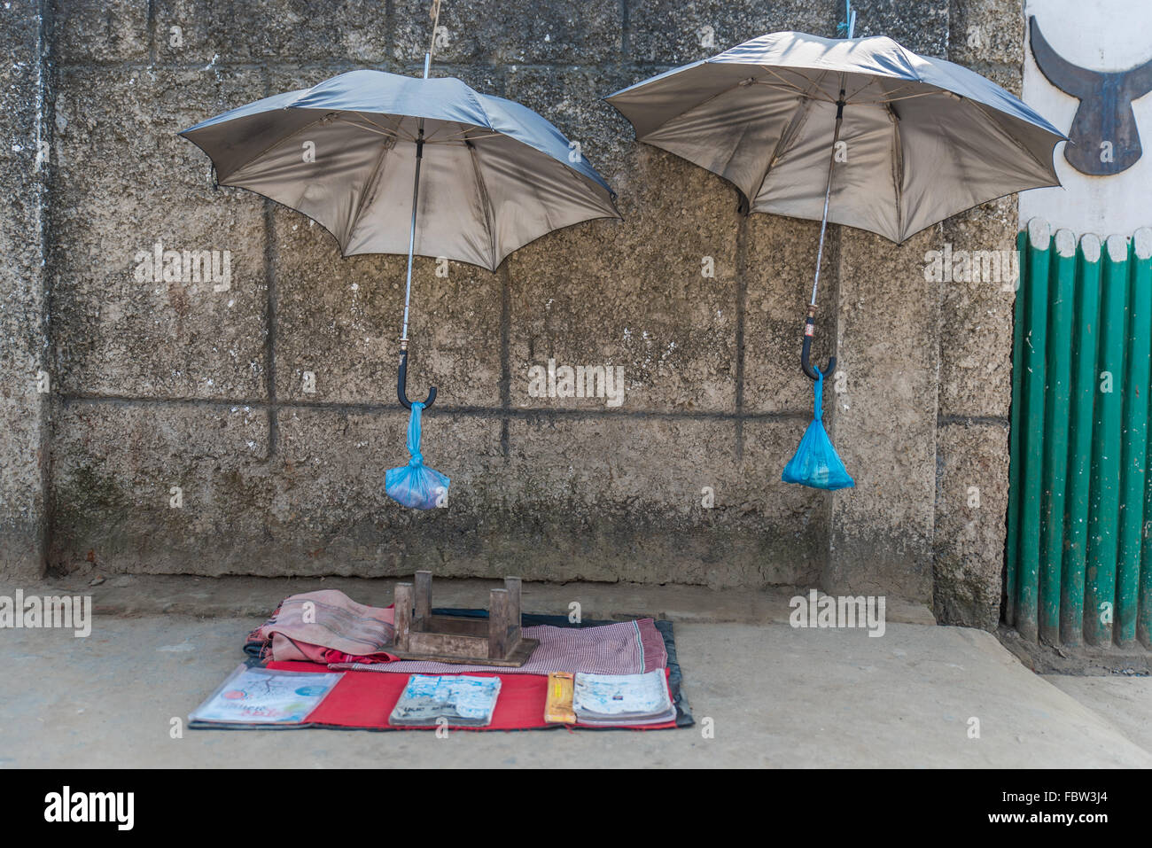 Sgabello capovolta su una coperta. Chiuso per pranzo. Due argento/grigio ombrelloni contro una superficie strutturata muro sporco con Naga corna. Il Nagaland Foto Stock