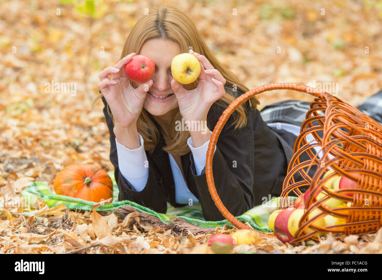 Giovane bella ragazza distesa sulle foglie in autunno la foresta, si trova accanto a un cesto di mele Foto Stock