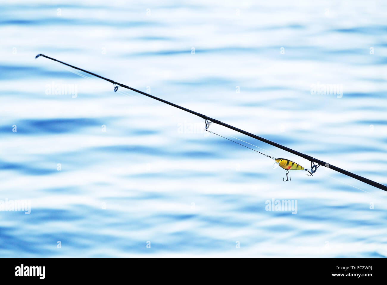 Canna da pesca e affrontare in blu sullo sfondo di acqua Foto Stock