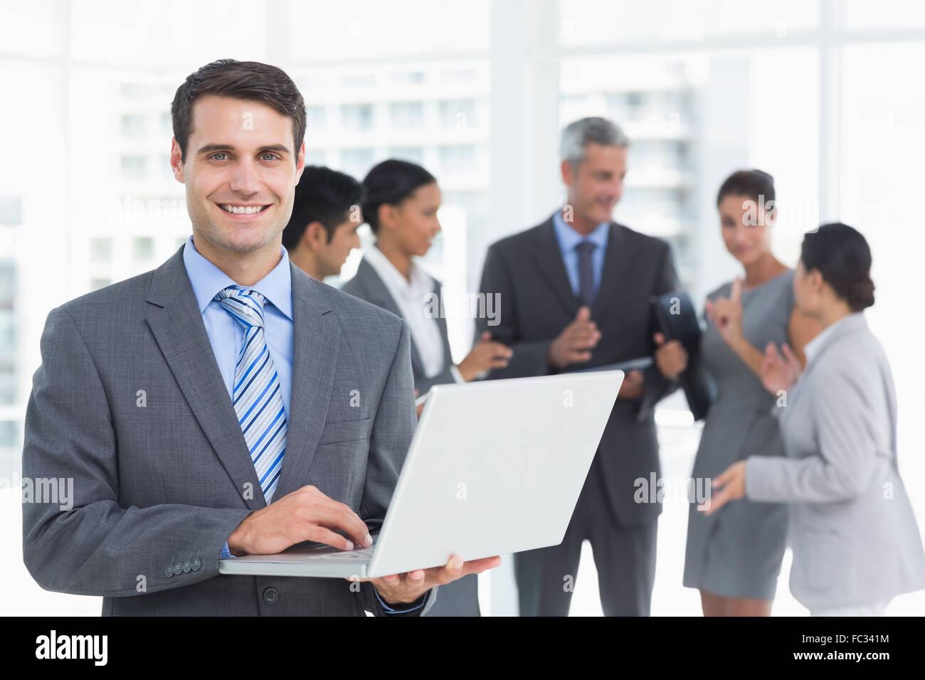 Uomo d affari con computer portatile con i colleghi dietro Foto Stock