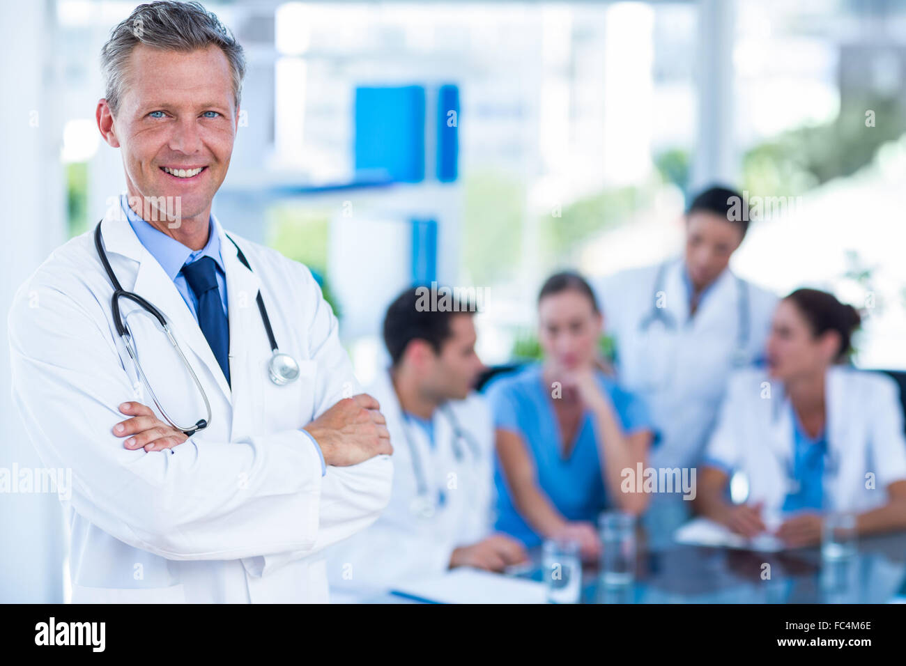 Medico sorridente in telecamera con i colleghi dietro Foto Stock