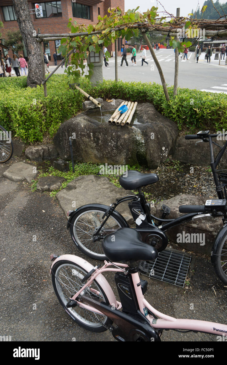 Biciclette elettriche a una fiera di strada a Takayama in Giappone con la fontana del santuario Foto Stock