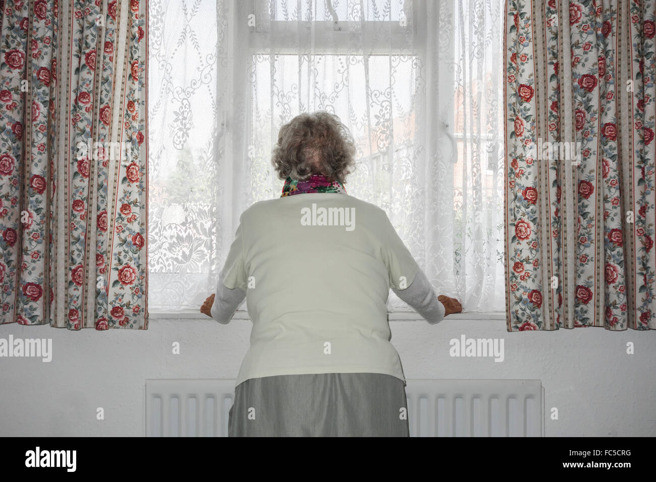 Donna di novanta anni con mano sul radiatore che guarda fuori dalla finestra. REGNO UNITO. Coronavirus, autoisolamento, distanza sociale, quarantena... concetto Foto Stock