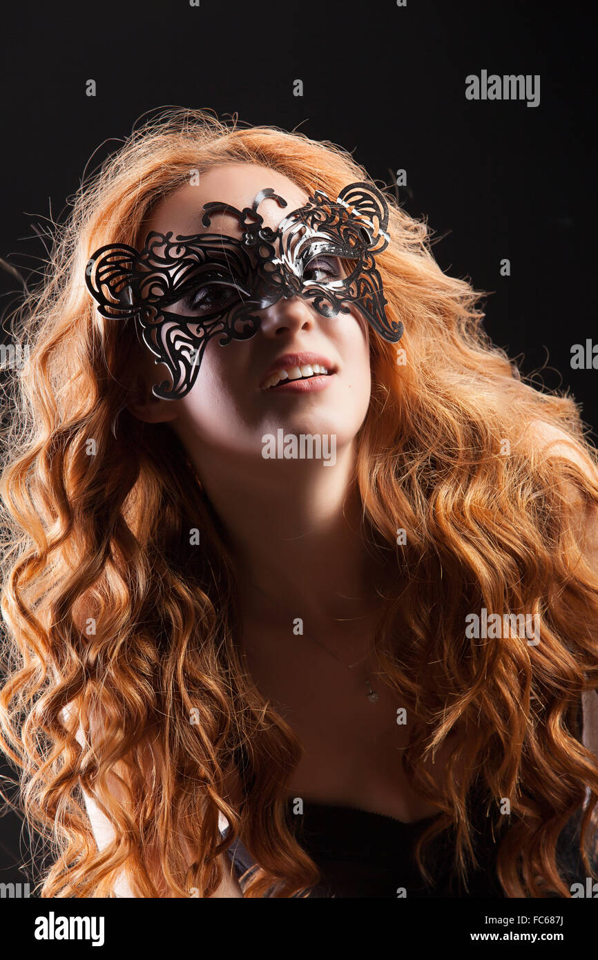 Giovani Red- donna dai capelli in una maschera nera Foto Stock