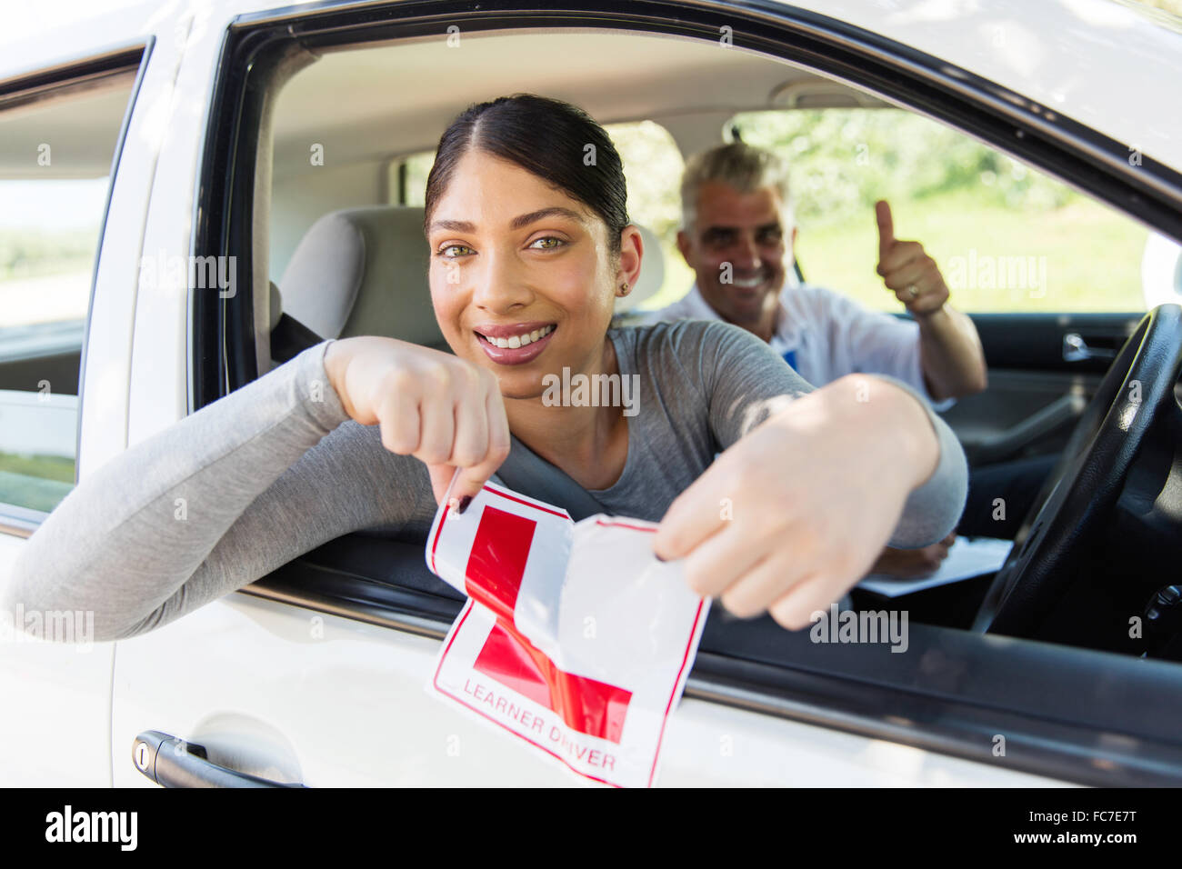 Felice ragazza seduta in auto la lacerazione di una L segno dopo aver ottenuto la sua patente di guida Foto Stock