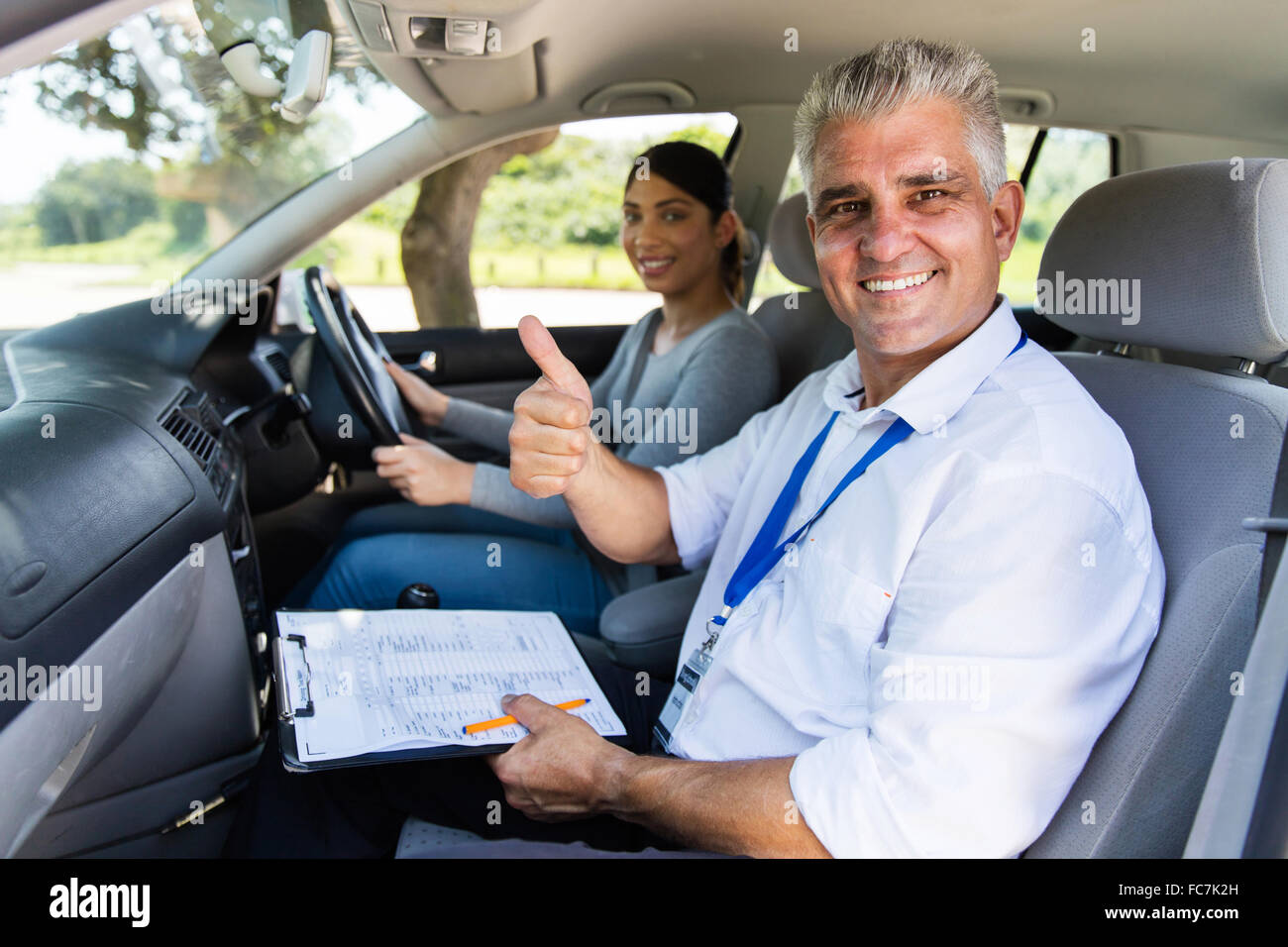Sorridente maschio senior istruttore di guida di una vettura con allievo conducente dando pollice in alto Foto Stock