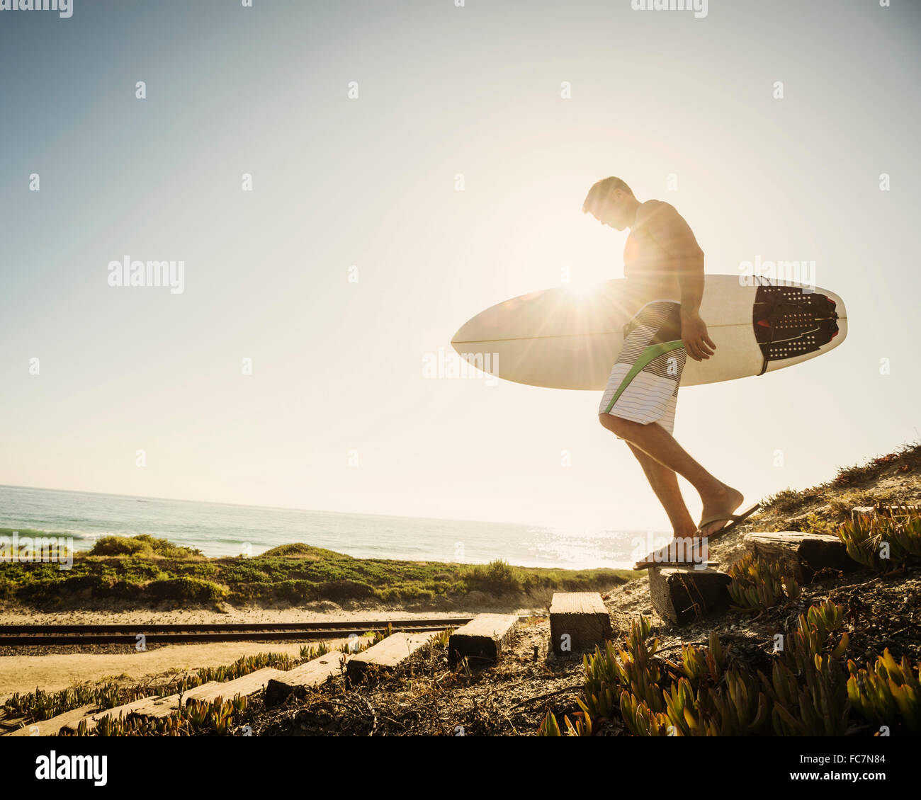Uomo caucasico che trasportano le tavole da surf in spiaggia Foto Stock
