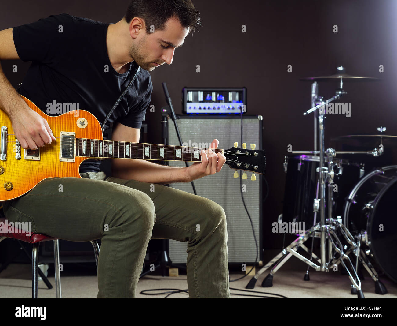 Foto di un uomo nel suo fine 20's seduto sul palco a suonare la chitarra. Foto Stock