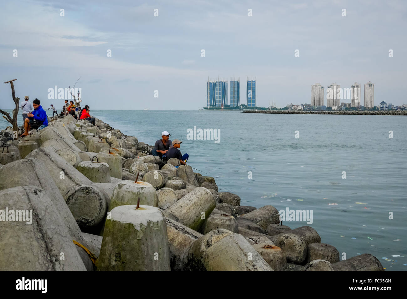 Persone che pescano da strutture di tetrapod, che stanno proteggendo il porto di pesca di Muara Angke come rompigonda a Penjaringan, Jakarta, Indonesia. Foto Stock