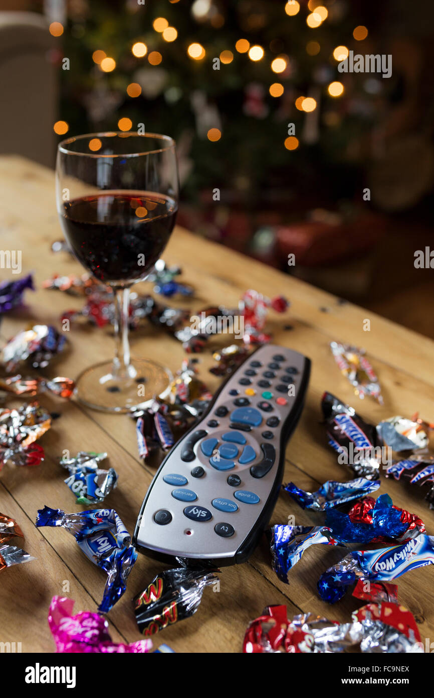Telecomando tv circondato da confezioni di caramelle e un bicchiere di vino a Natale. Foto Stock