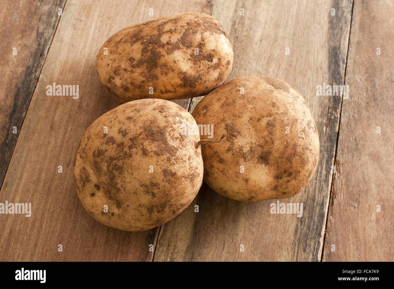Tre Unwashed patate su una tavola di legno Foto Stock