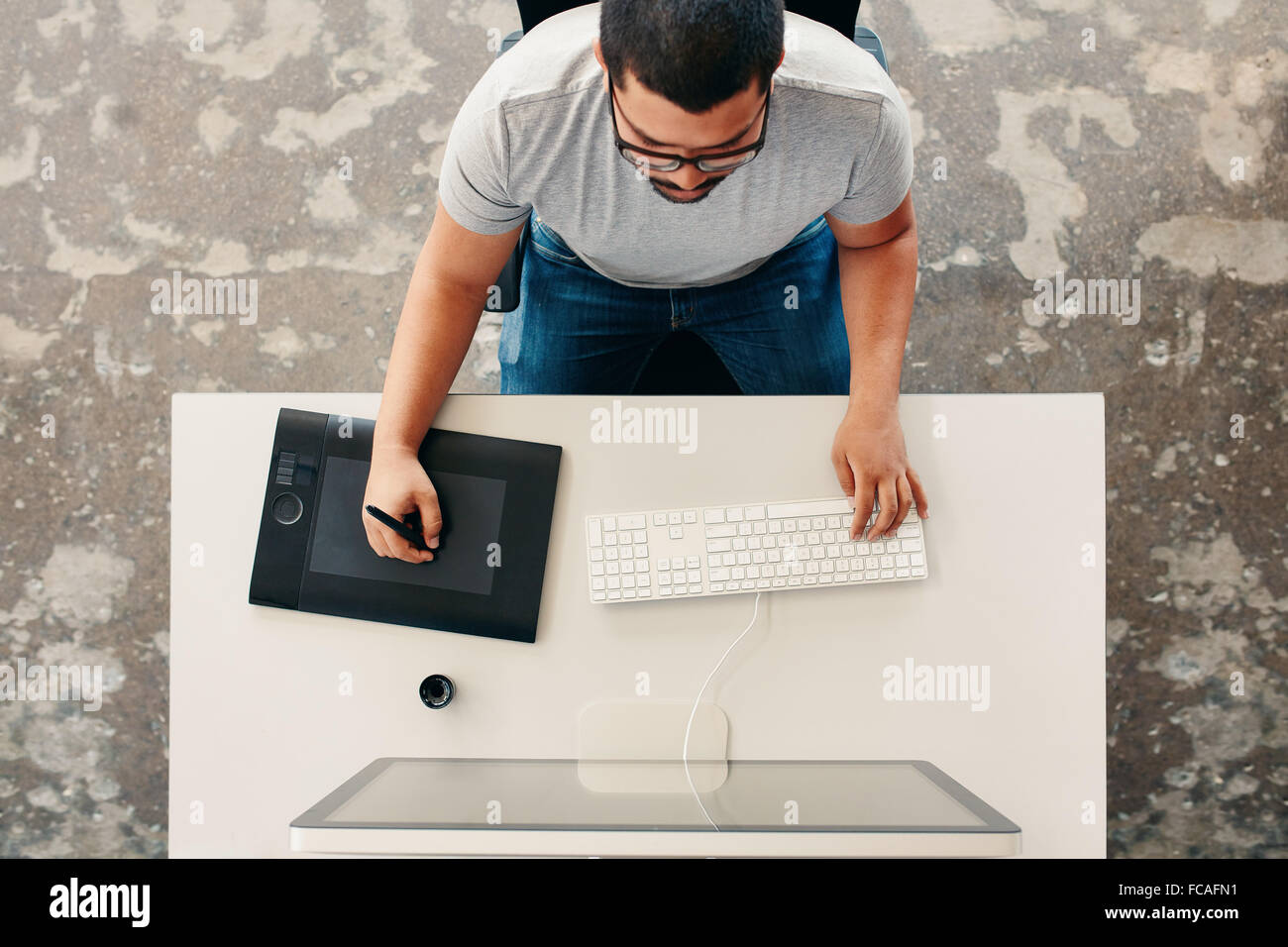 Vista dall'alto di un maschio di graphic designer con tavoletta grafica digitale e di desktop in ufficio. Editor seduto alla sua scrivania disegno Foto Stock