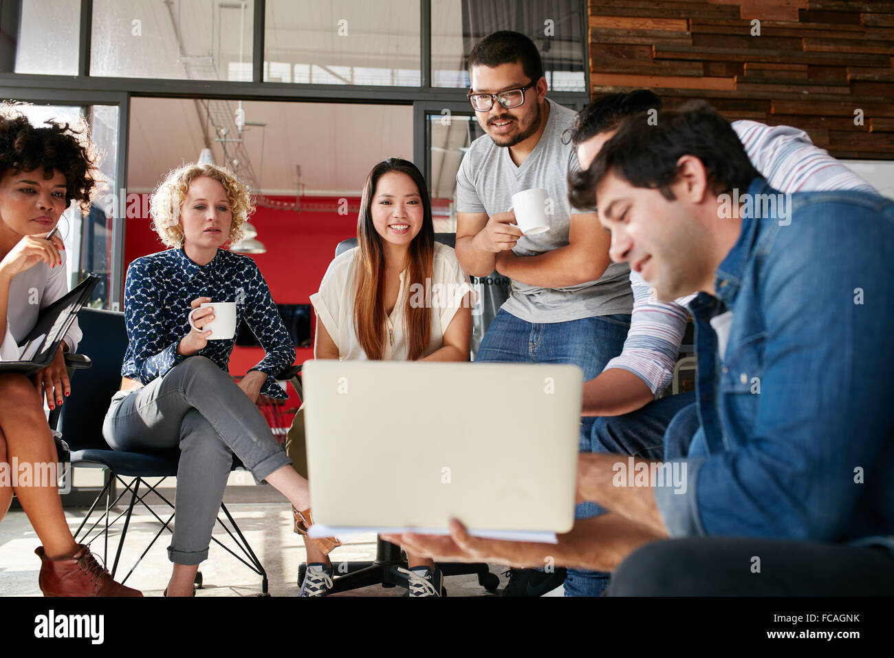 Team di persone creative guardando collega mostra piano di progetto sul suo computer portatile. Diversi gruppi di giovani aventi una riunione Foto Stock