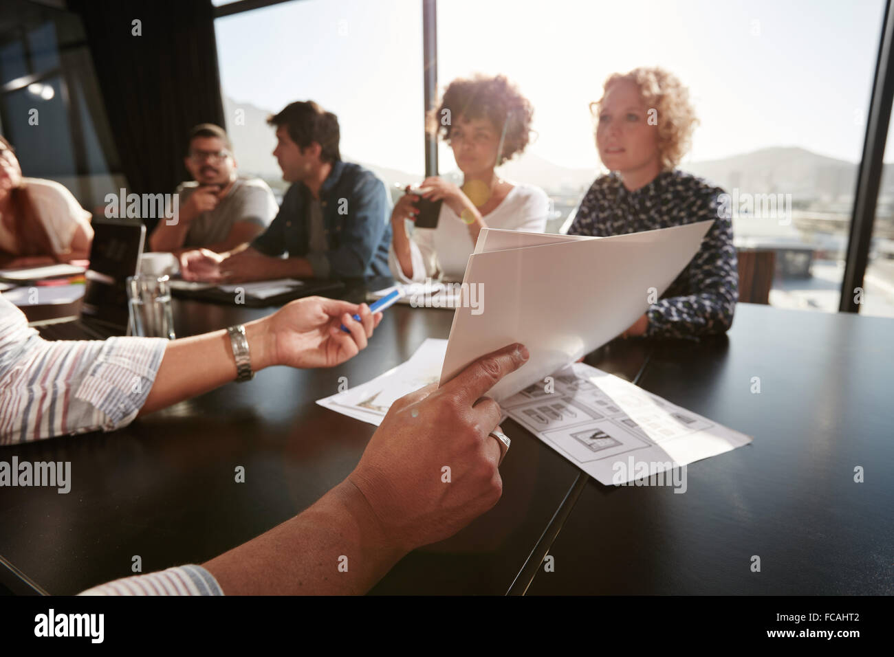 Carte nella mani del giovane uomo che spiega il business plan per il suo team creativo. I professionisti creativi riunione in ufficio. Foto Stock
