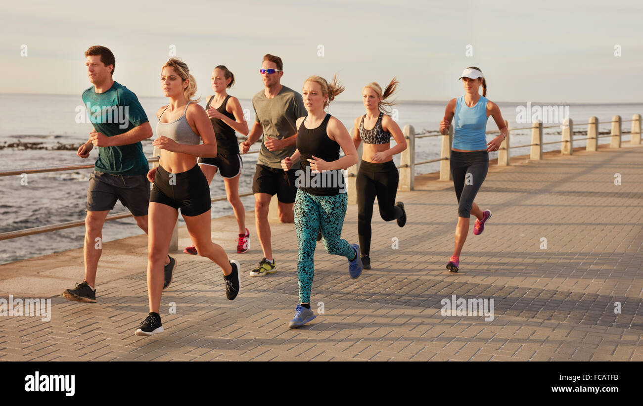 Ritratto di giovani che corre lungo il lungomare dall'oceano. Montare i giovani uomini e donne in esecuzione della formazione all'aperto da th Foto Stock