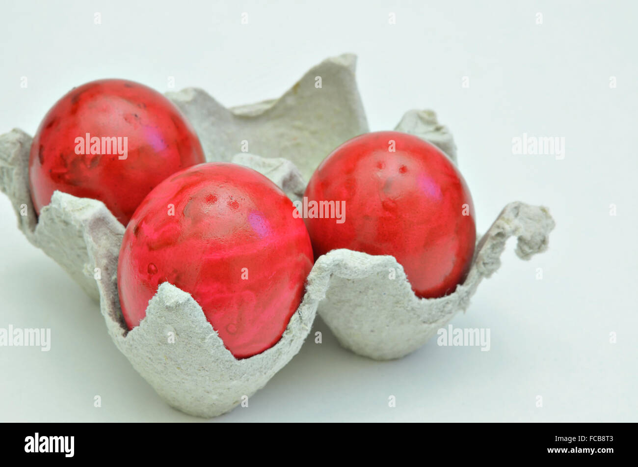 Tre rosso uova di pasqua in una scatola di cartone, vicino, isolati su sfondo bianco, orizzontale Foto Stock