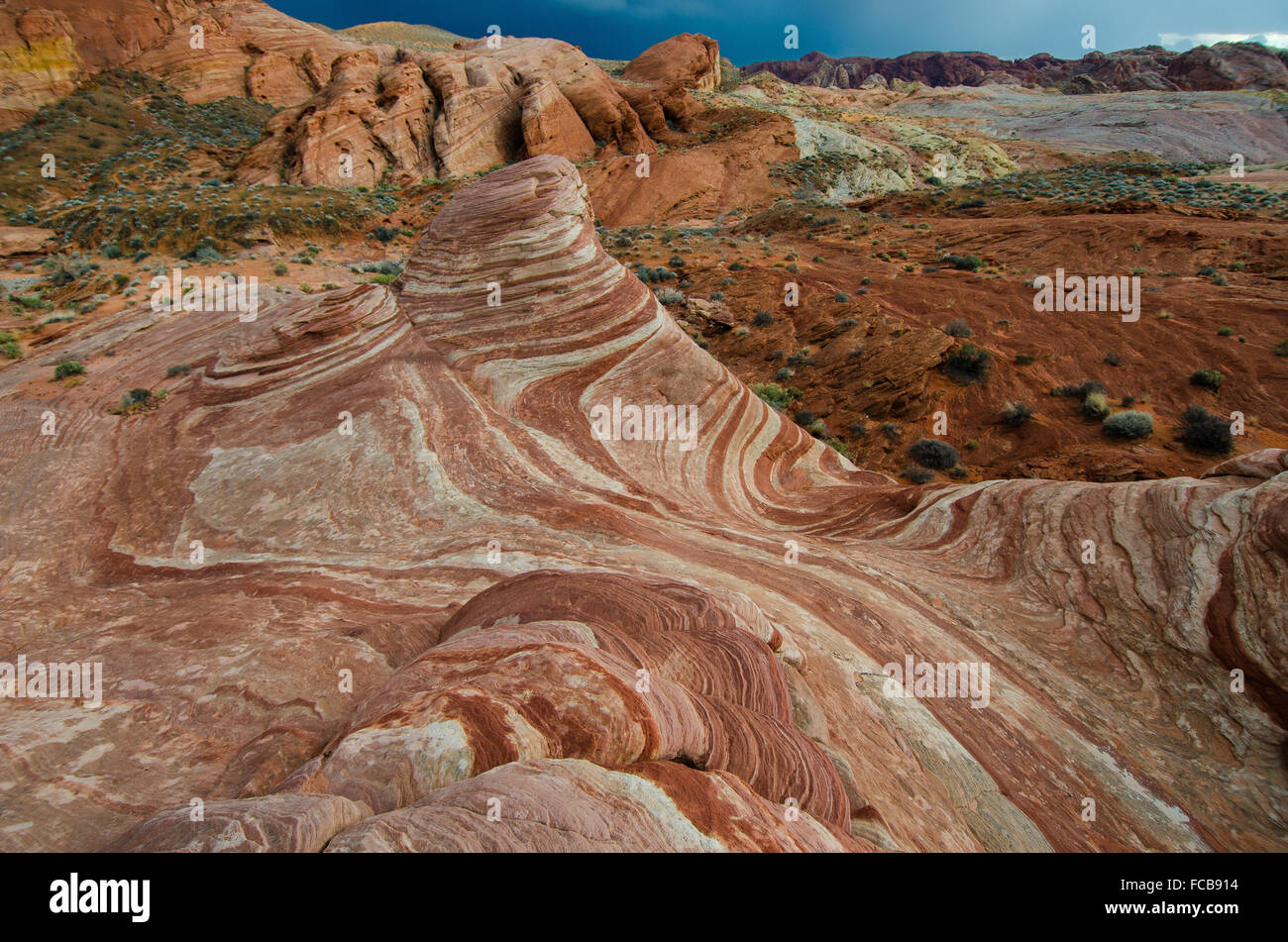 Dark nuvole infausto glide passato la roteazione red rock striature della Valle di Fire State Park. Foto Stock