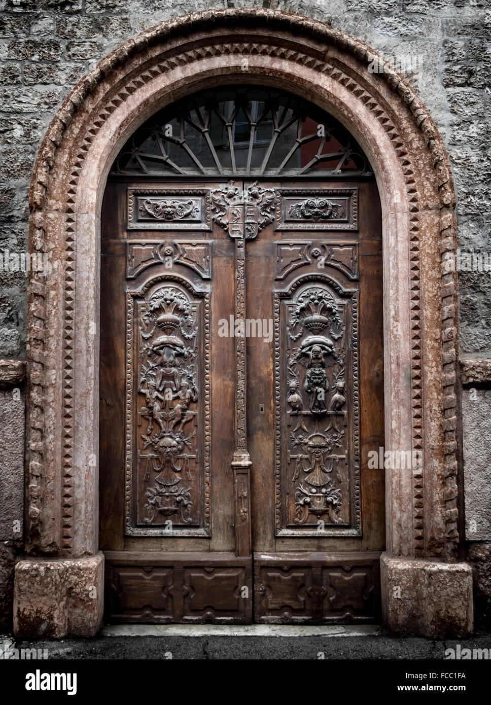 Antico cancello in legno con volta in pietra scolpita con figure demoniaca. Foto Stock