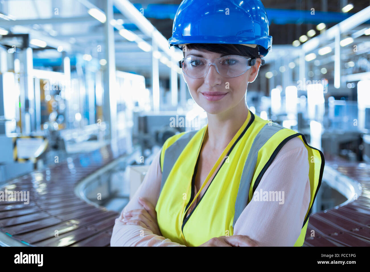 Ritratto fiducioso lavoratrice con hard-cappello e occhiali protettivi in fabbrica Foto Stock