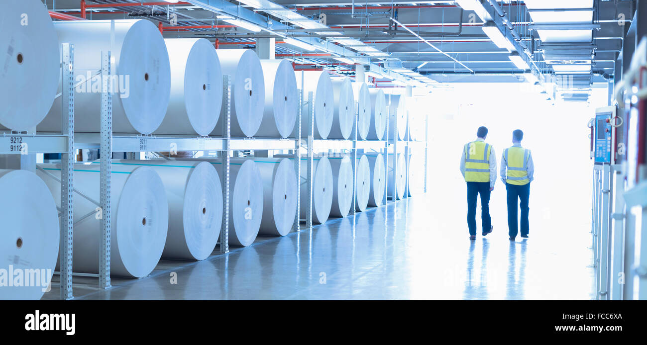 Lavoratori in abbigliamento riflettivo a piedi lungo i grandi bobine di carta in impianto di stampa Foto Stock