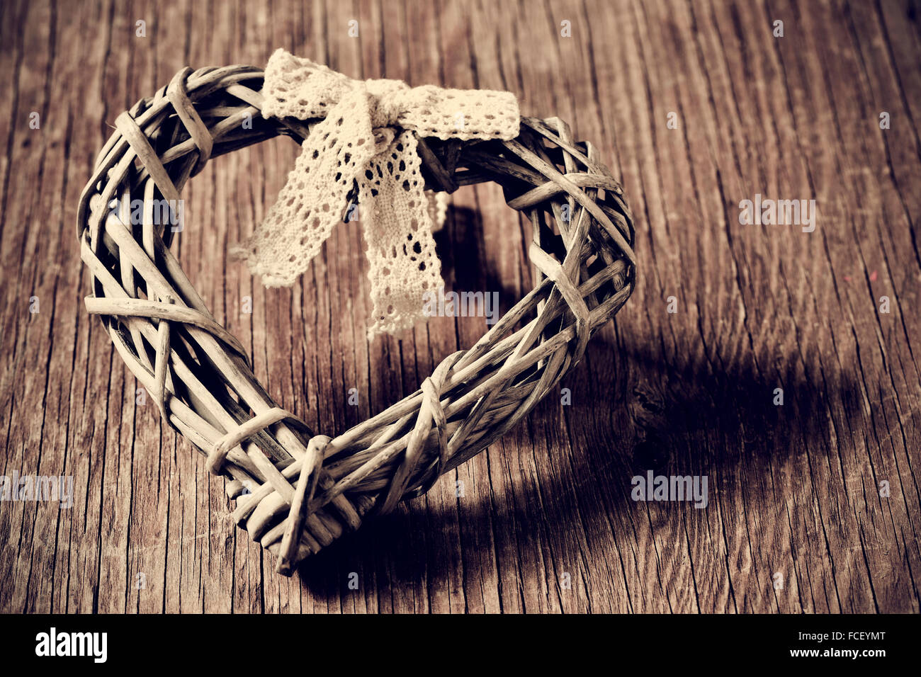 A heart-shaped ornamento realizzato con legato alle fibre naturali e una prua di pizzo su un rustico di una superficie di legno, in seppia tonificante Foto Stock