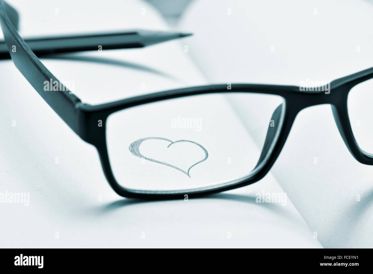 Un cuore disegnato in un notebook vista attraverso la lente di plastica nero-bordati di occhiali, in bicromia Foto Stock