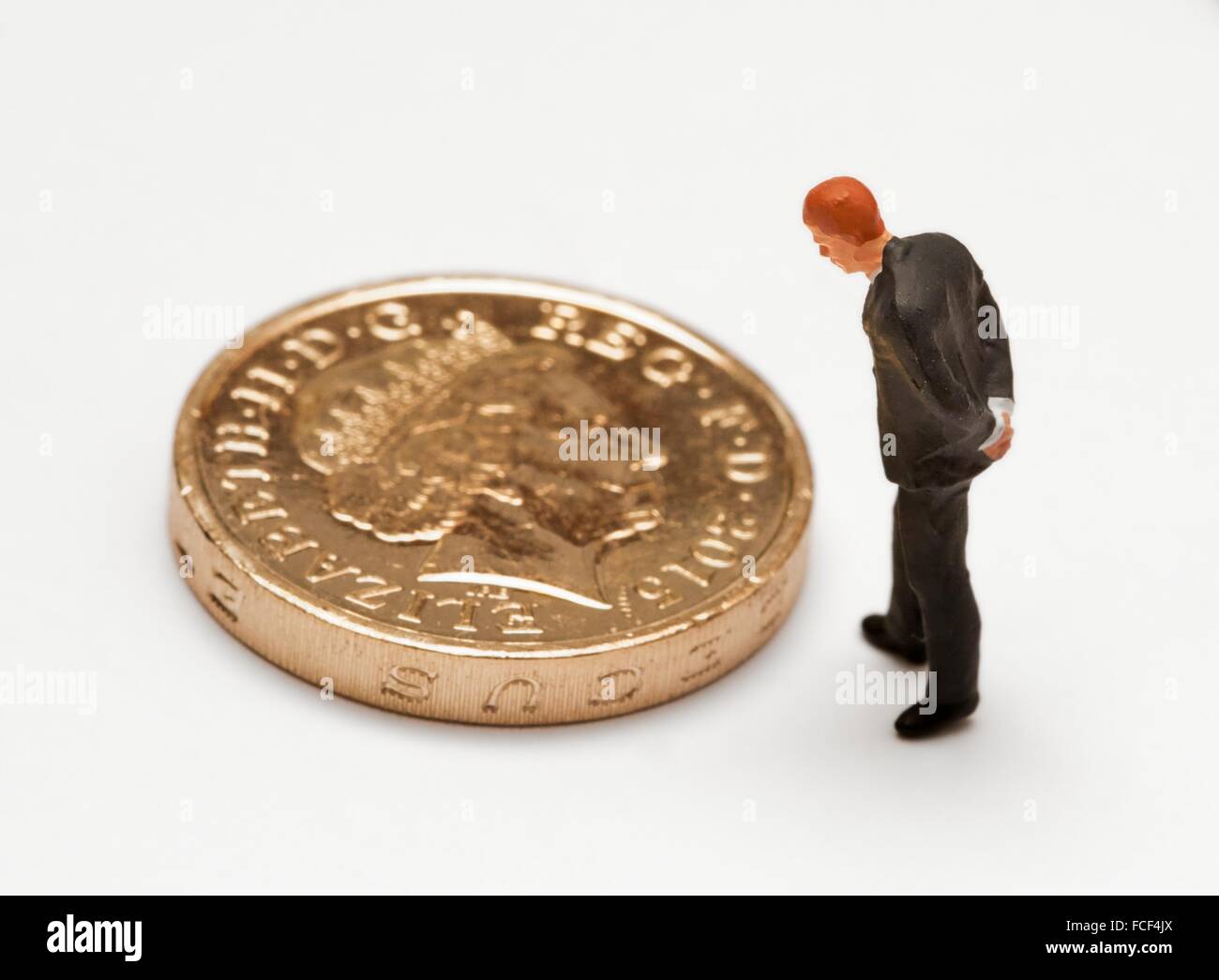Una statuetta in miniatura uomo in una tuta guardando uno britannico pound coin. Foto Stock