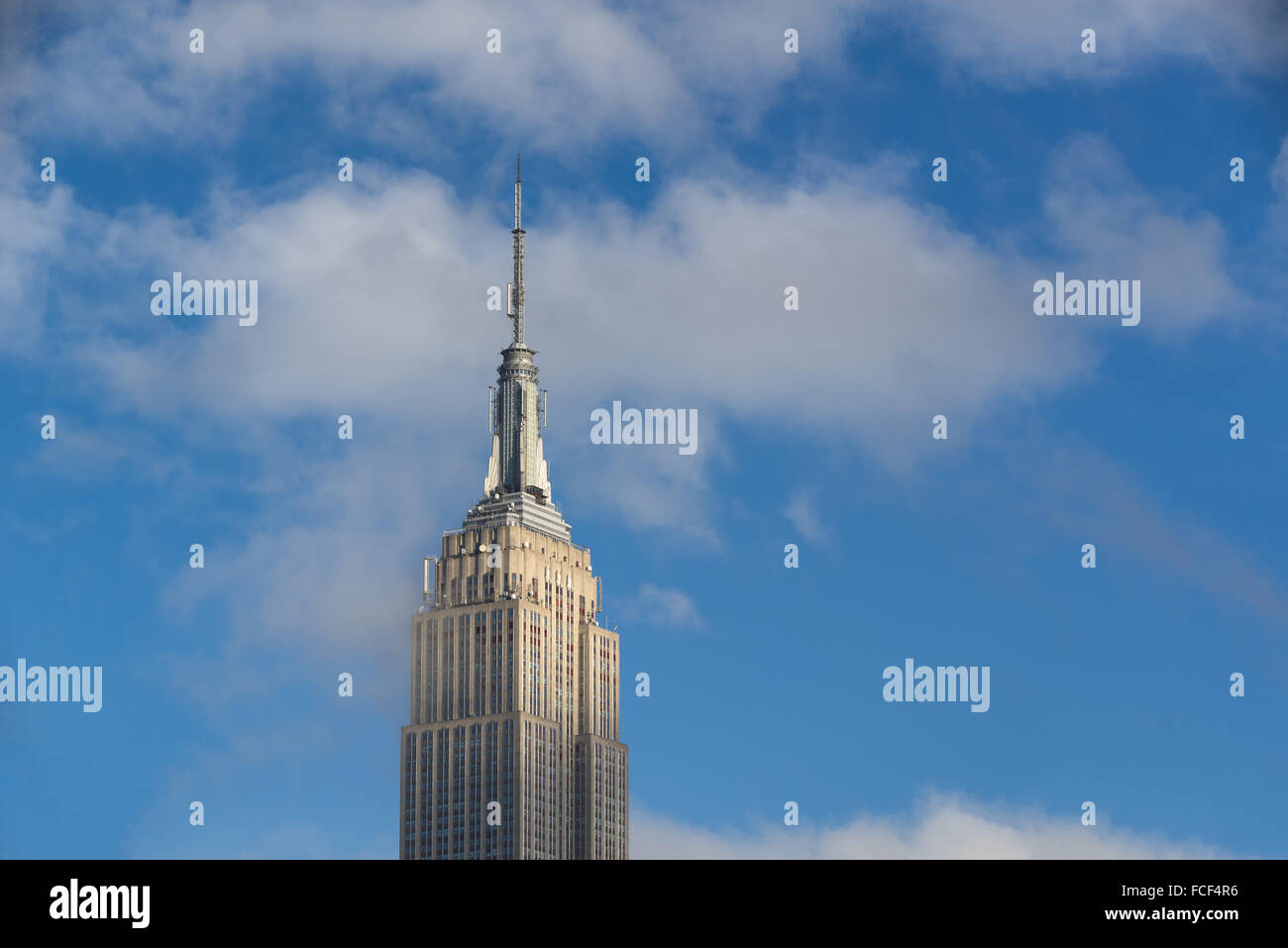 Parte superiore dell'Empire State Building grattacielo in un nuvoloso cielo blu con la nebbia nella luce del pomeriggio. Midtown Manhattan, a New York City Foto Stock