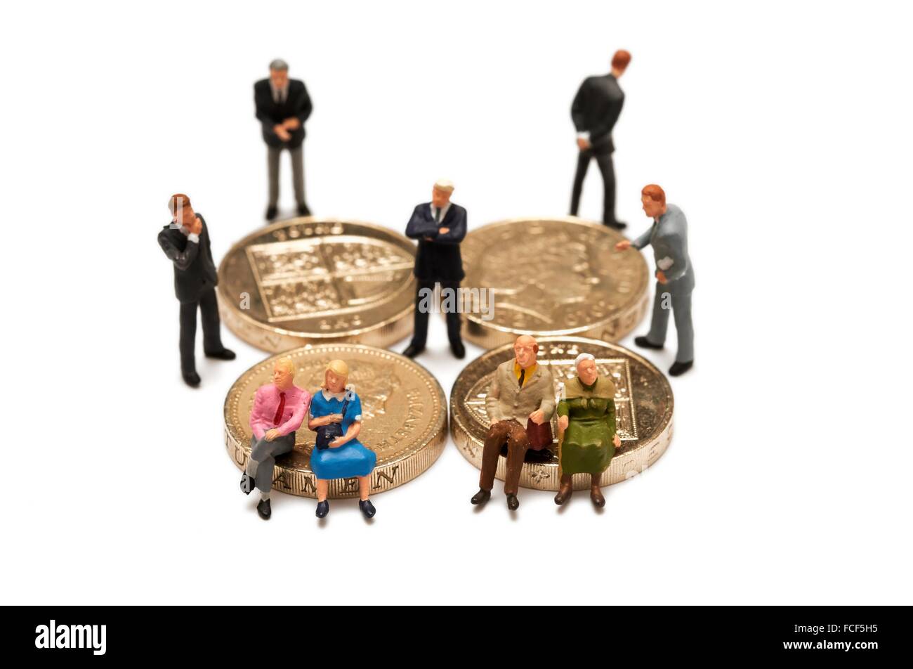 2 coppie in miniatura seduti sulle monete Britanniche circondato da advisor finanziario di tute concetto. Foto Stock