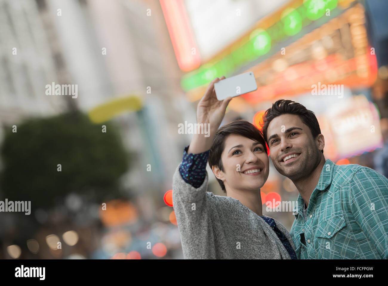 Un giovane uomo e donna su una strada di città prendendo un selfy con uno smart phone. Foto Stock