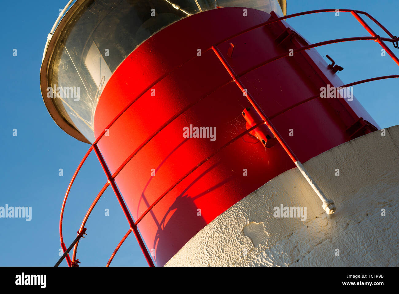 Dettagliata vista di inclinazione di un faro alto con colori bianco e rosso, illuminata dal luminoso e golden la luce del sole al tramonto Foto Stock