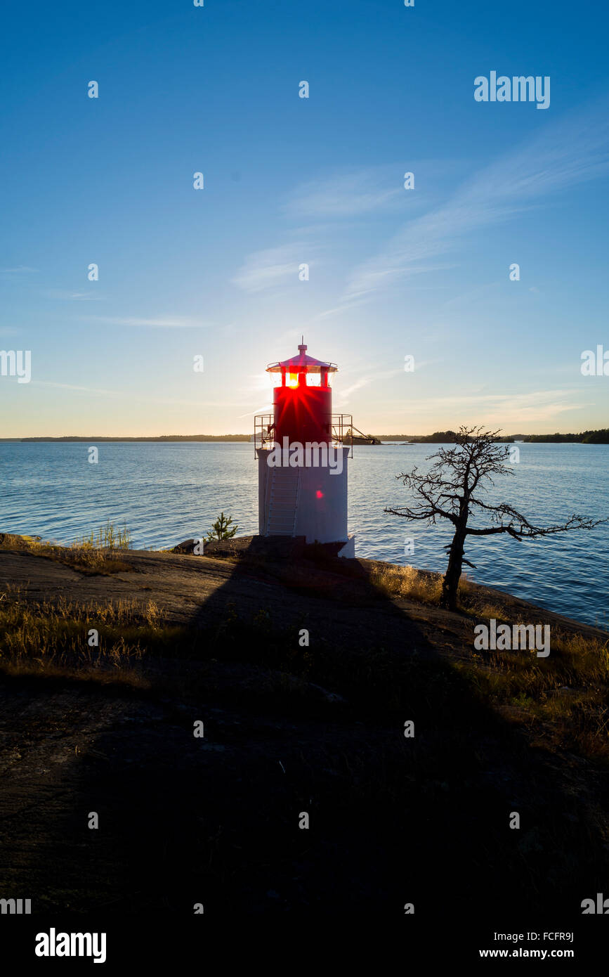 Sunray brillare attraverso un faro sulla costa rocciosa nell'isola svedese Yxlan nell arcipelago vicino a Stoccolma al tramonto Foto Stock