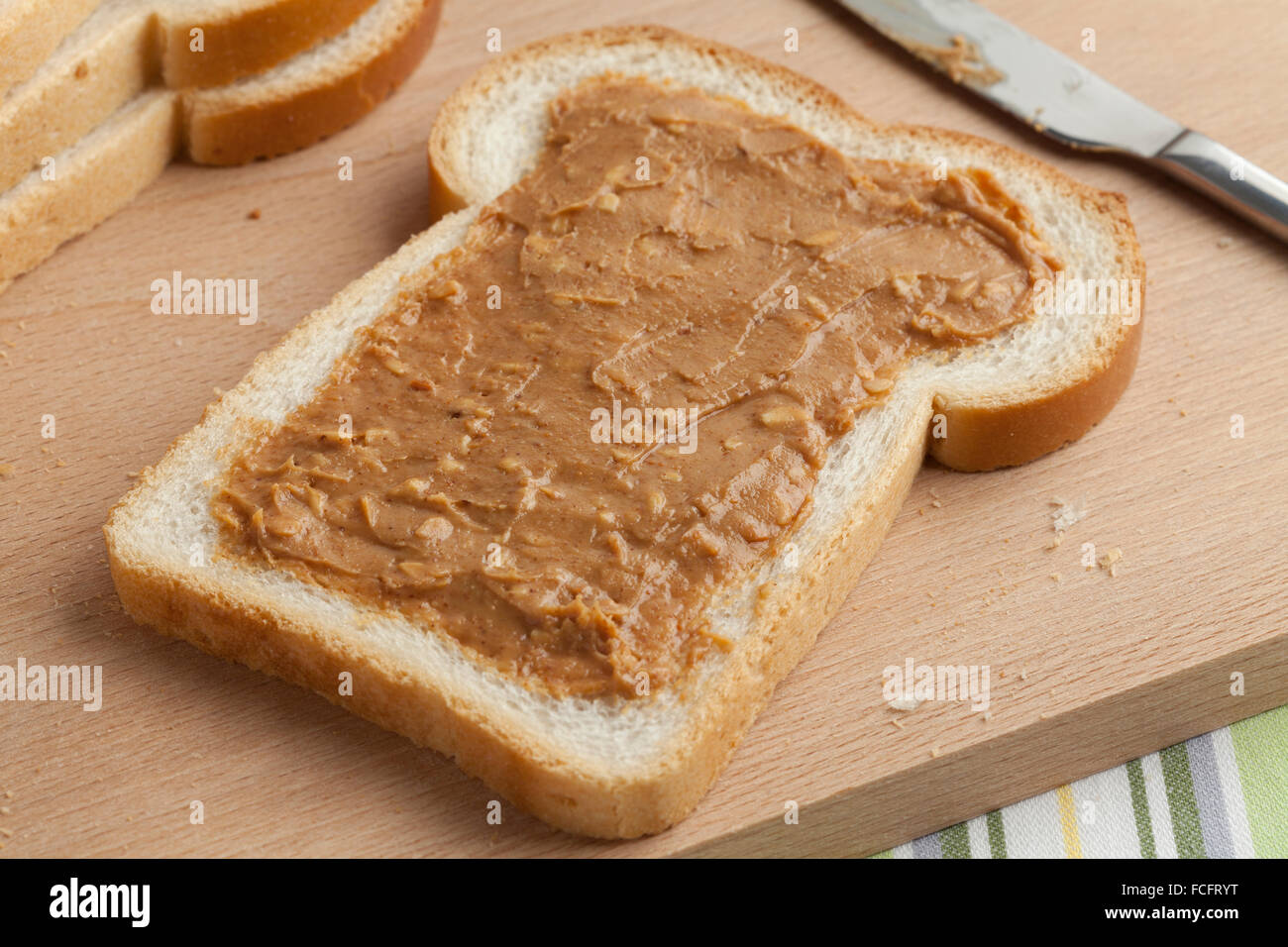 Fetta di pane bianco con burro di arachidi su di un tagliere di legno Foto Stock