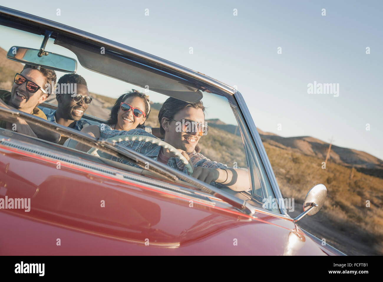 Un gruppo di amici in un rosso open top convertibile auto classica in un viaggio su strada. Foto Stock