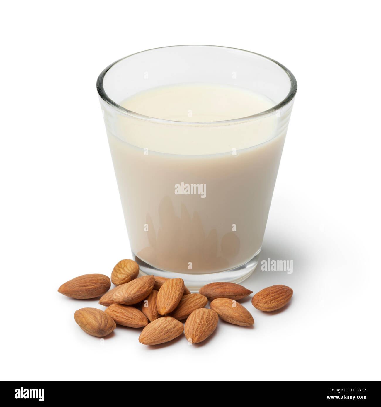 Un bicchiere di latte di mandorla con un mucchio di mandorle su sfondo bianco Foto Stock