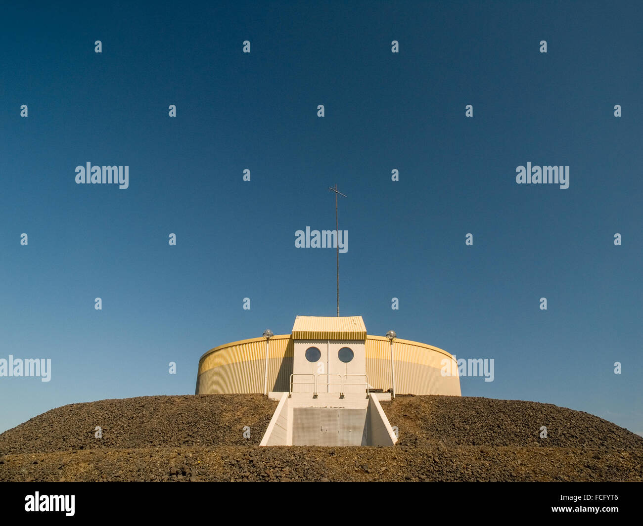 Circolare giallo industriale e edificio grigio sulla parte superiore della piattaforma di ghiaia contro un blu cielo chiaro vicino a Keflavik Islanda. Foto Stock