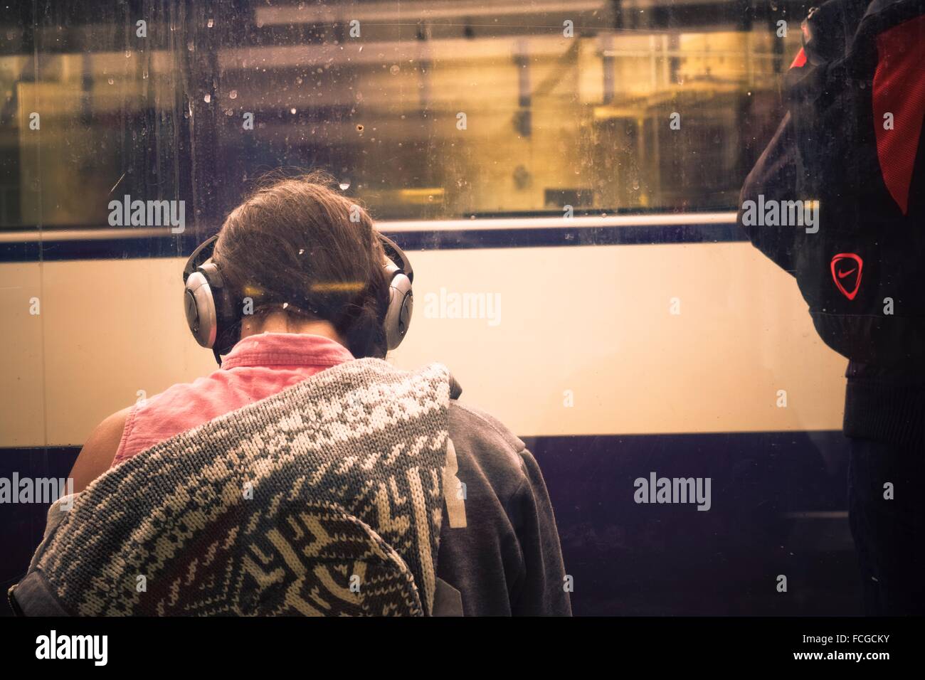 Giovane donna torna con le cuffie sull'ascolto di musica. Sullo sfondo la vettura di un treno in movimento. London, England, Regno Foto Stock