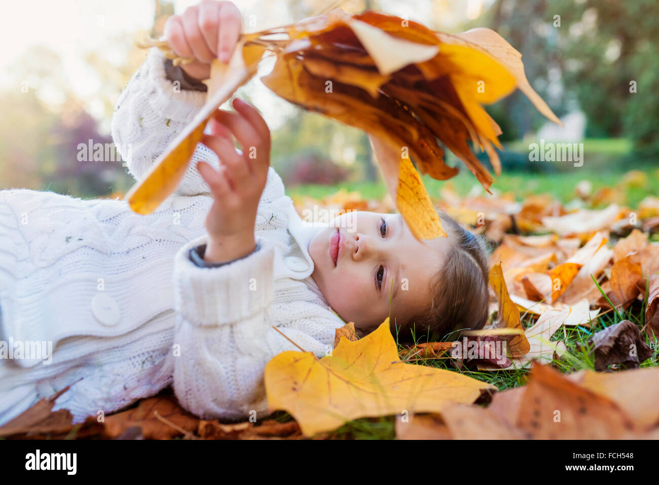 Ragazza distesa in prato autunnale trattenere foglie Foto Stock